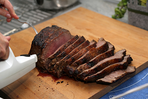 electric carving knife slicing a roast on a wood cutting board